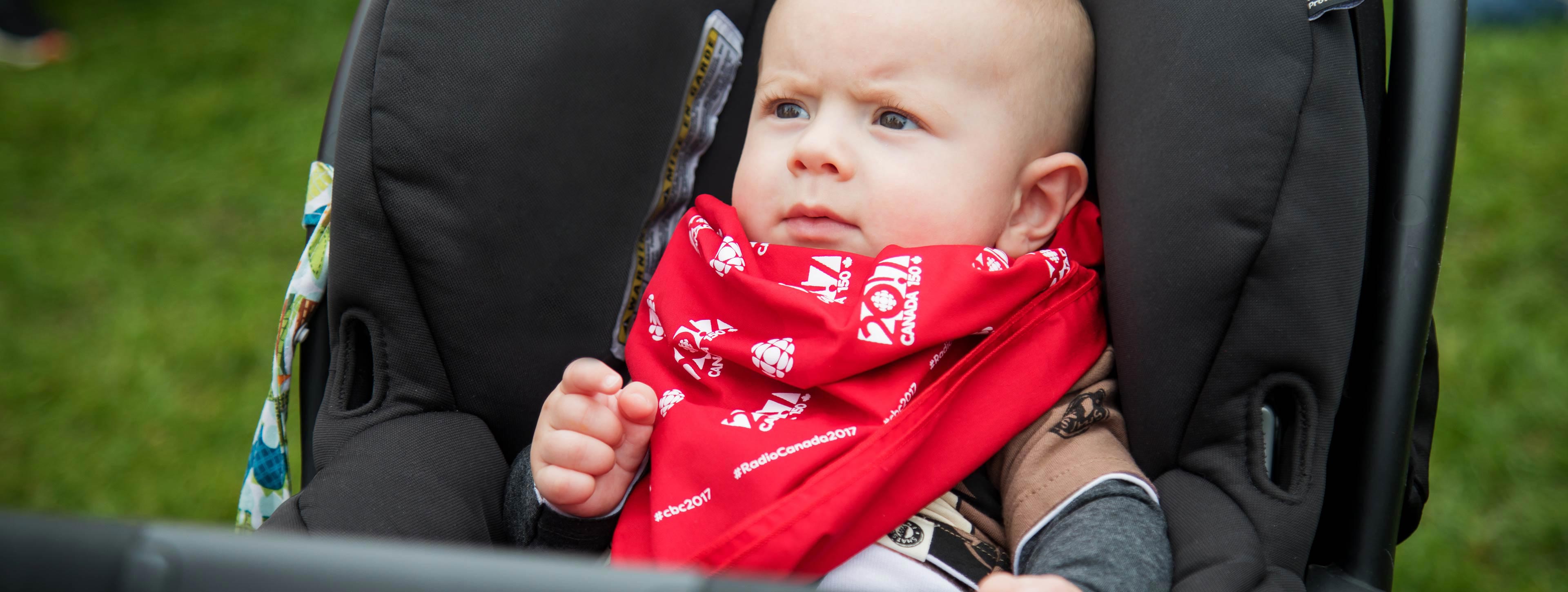 A baby wearing a CBC Canada 150 red scarf.
