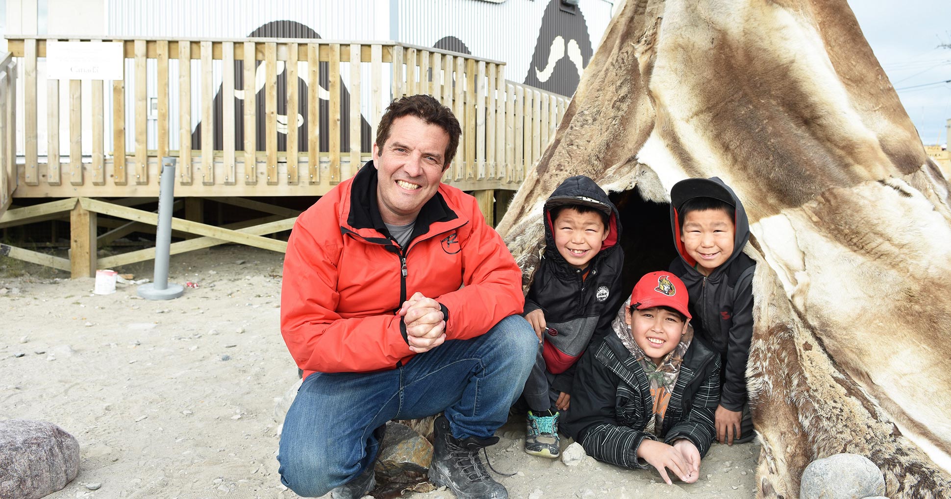 Rick Mercer smiles next to three children from Nunavut. 

